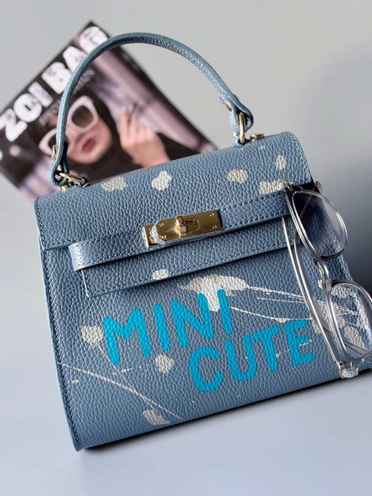 Designová modrá kožená kabelka Zoi Bag s ručně psaným nápisem a s cákanci barvou. Zapínání pomocí otočného zlatého zámku.