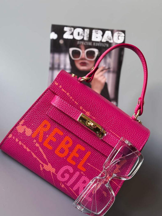 Designová růžová kožená kabelka Zoi Bag s ručně psaným nápisem "Rebel Girl" a cákanci barvou.
