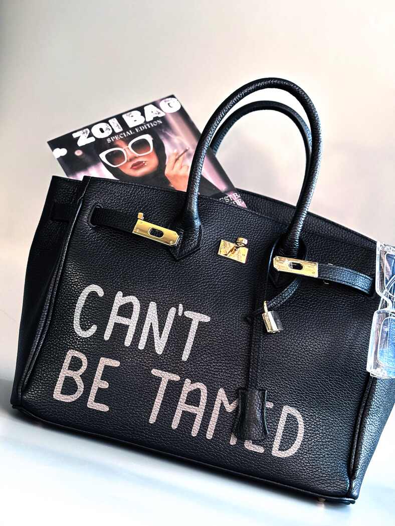 Černá kožená kabelka s ručně psaným nápisem "Can't be tamed"