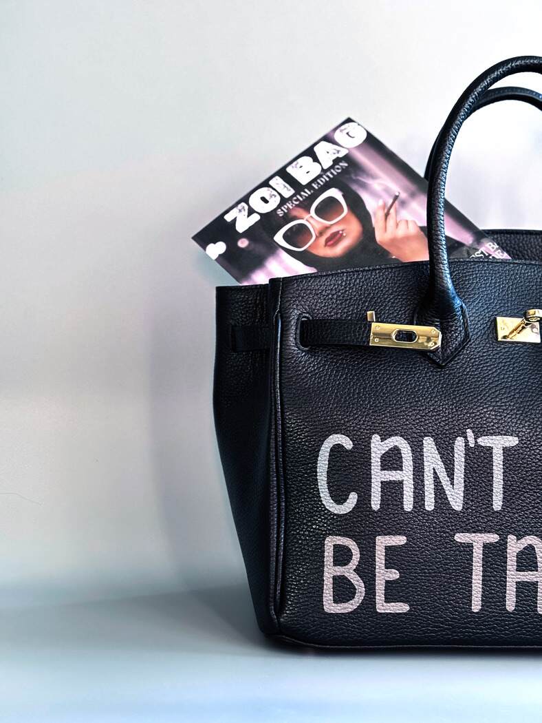 Černá kožená kabelka s ručně psaným nápisem "Can't be tamed"