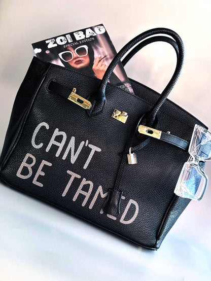 Černá kožená kabelka s ručně psaným nápisem "Can't be tamed"