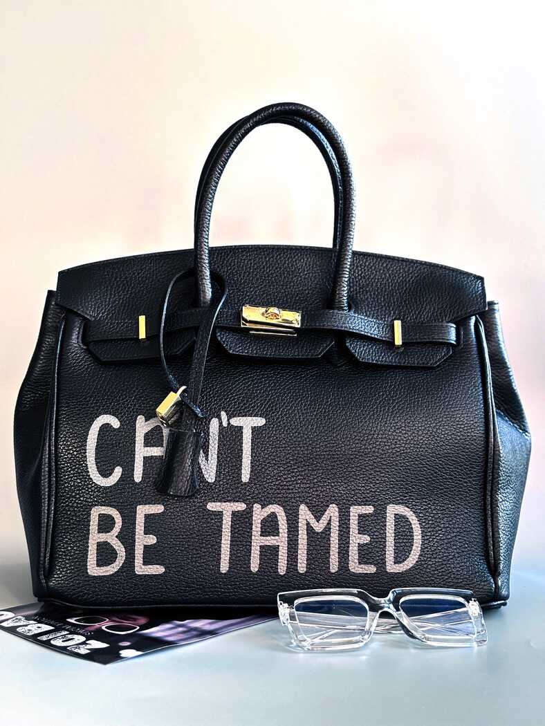 Černá kožená kabelka s ručně psaným nápisem "Can't be tamed"