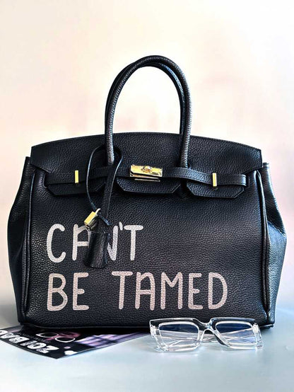 Černá kožená kabelka s ručně psaným nápisem "Can't be tamed"