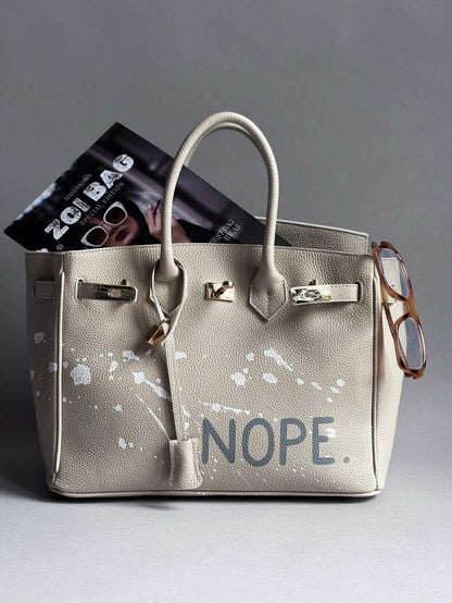 Béžová kožená kabelka Zoibag s ručně malovaným nápisem “Nope” a cákanci barvou.