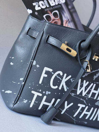 Detail ručně malovaného nápisu a uměleckými cákanci barvou na šedé kožené kabelce od Zoibag. 