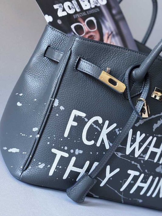 Detail ručně malovaného nápisu a uměleckými cákanci barvou na šedé kožené kabelce od Zoibag. 