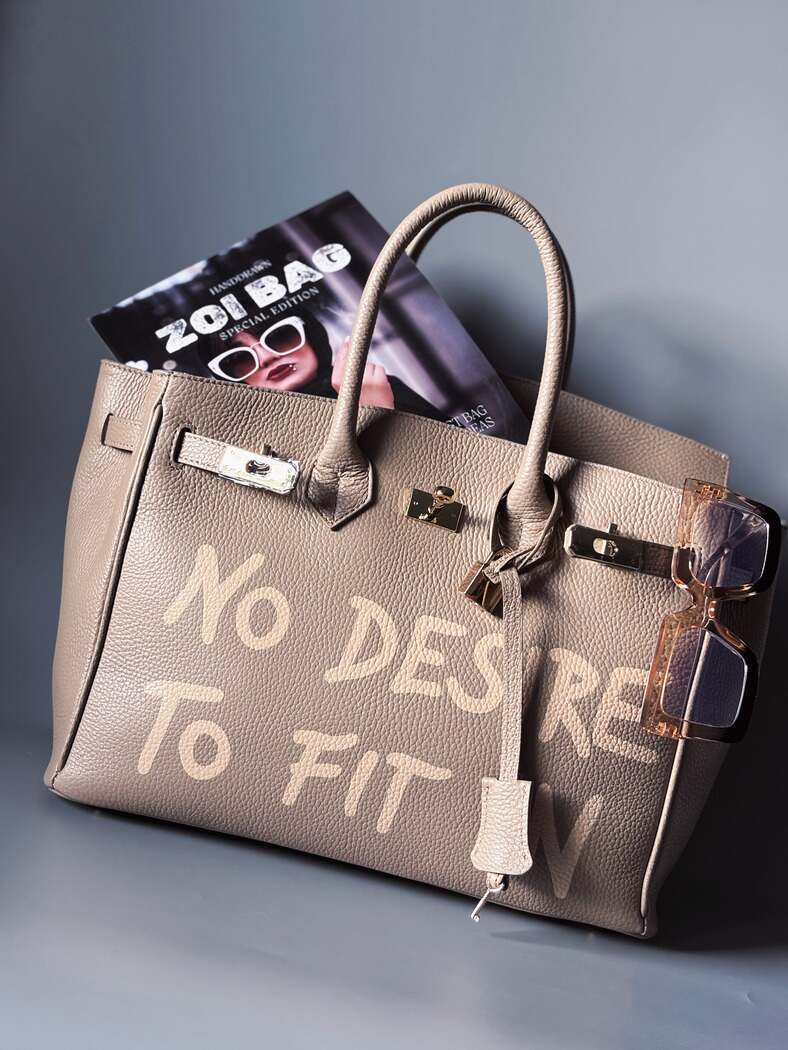 Luxusní designová béžová kabelka vyrobená z kvalitní italské kůže s ručně psaným nápisem. Ikonické zapínání na zámek s klíčkem.