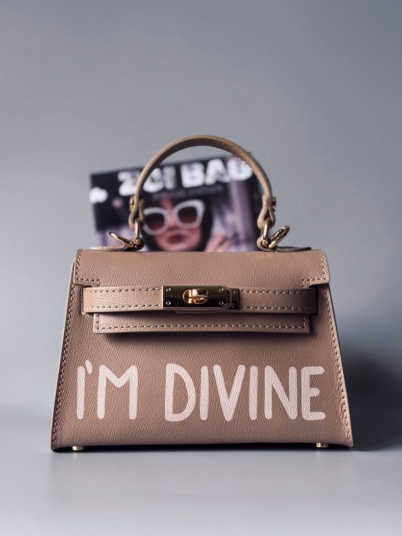 Designová luxusní béžová kabelka s ručně psaným nápisem, elegantním otočným zámkem a odnímatelným crossbody popruhem.