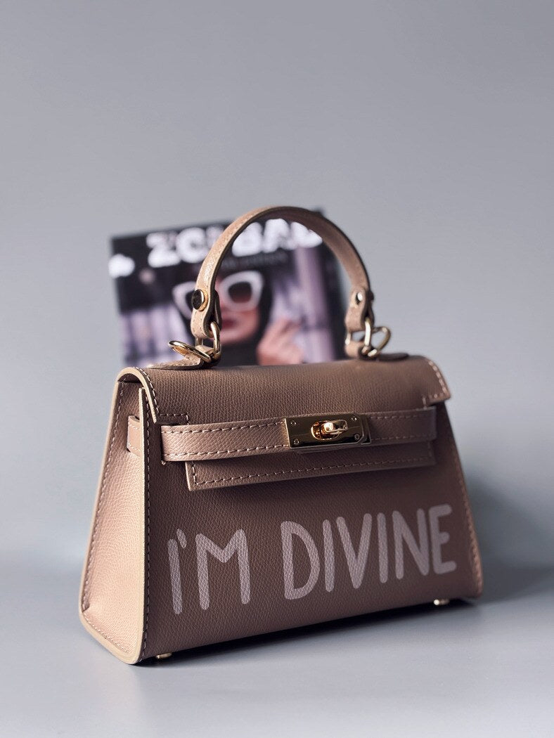 Designová luxusní béžová kabelka s ručně psaným nápisem, elegantním otočným zámkem a odnímatelným crossbody popruhem.