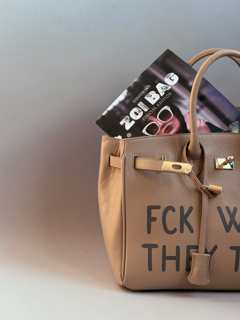 Béžová kožená shopper kabelka s ikonickým zapínáním na zámek a s originálním ručně malovaným nápisem. Detail nápisu.