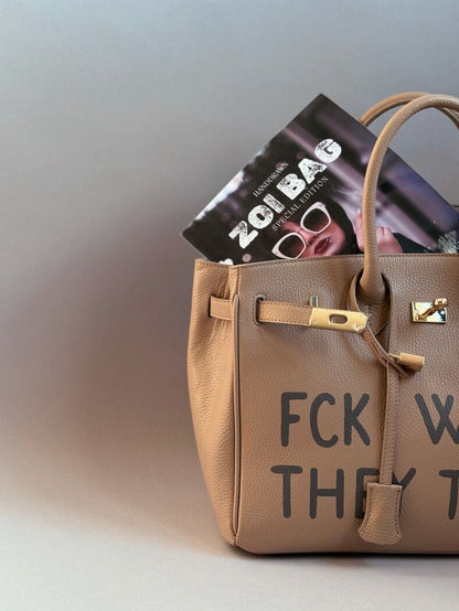 Béžová kožená shopper kabelka s ikonickým zapínáním na zámek a s originálním ručně malovaným nápisem. Detail nápisu.