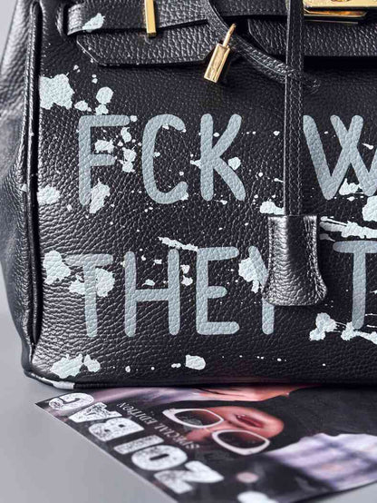 Luxusní designová kabelka Zoi Bag s ručně psaným nápisem a s cákanci barvou. Ikonické zapínání se zámkem a klíčkem. Detail nápisu.