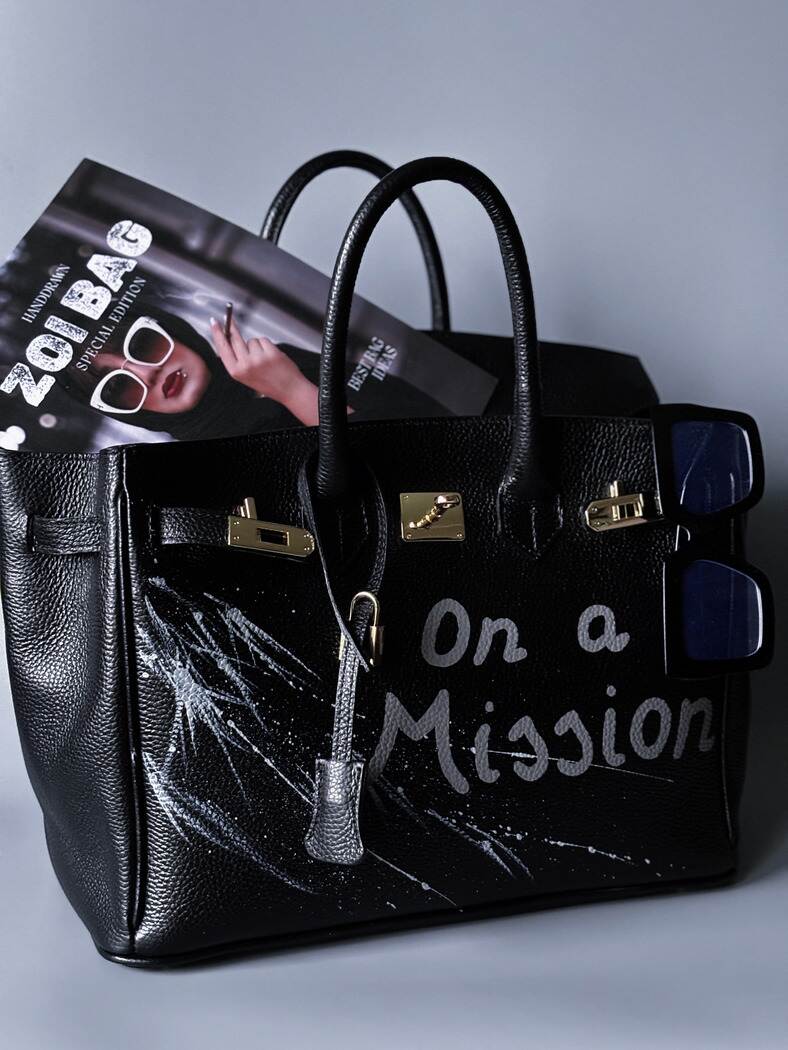 Černá kožená kabelka Zoi Bag s ručně psaným nápisem "On a Mision"  boku