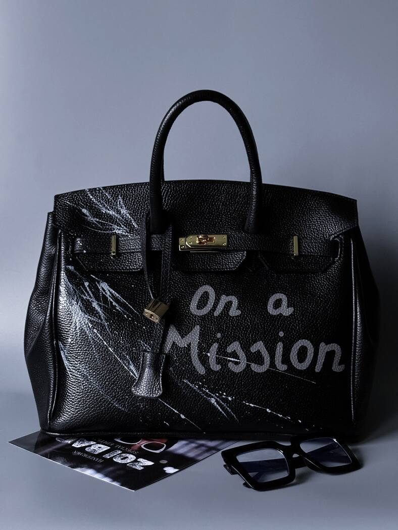 Černá kožená kabelka Zoi Bag s ručně psaným nápisem "On a Mision" zapnutá