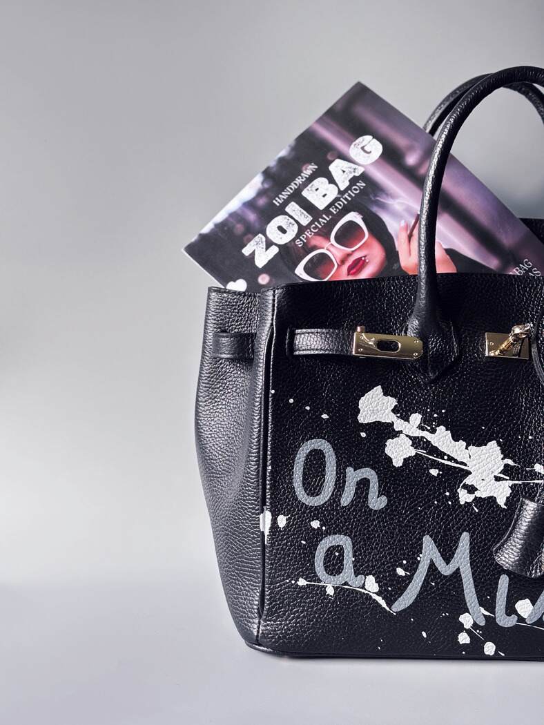 Designová černá kožená kabelka Zoi Bag s ručně psaným nápisem "On a Mission" a cákanci barvou. Zapínání zámkem turn-lock. Detail.