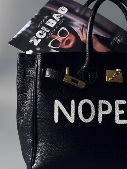 Černá kožená kabelka Zoi Bag s ručně psaným nápisem z pravé italské kůže se zapínáním pomocí ikonického zámku s klíčkem. Detail nápisu.