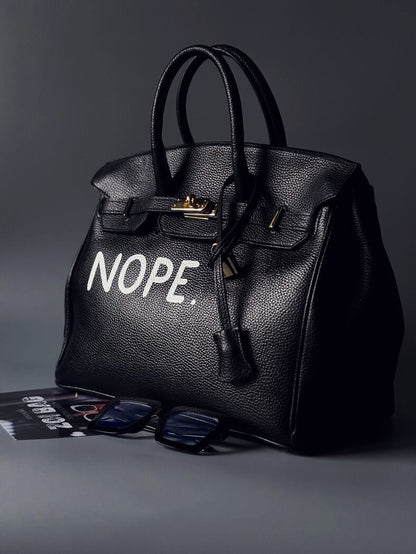 Černá kožená kabelka Zoi Bag s ručně psaným nápisem z pravé italské kůže se zapínáním pomocí ikonického zámku s klíčkem. Zapnutá.