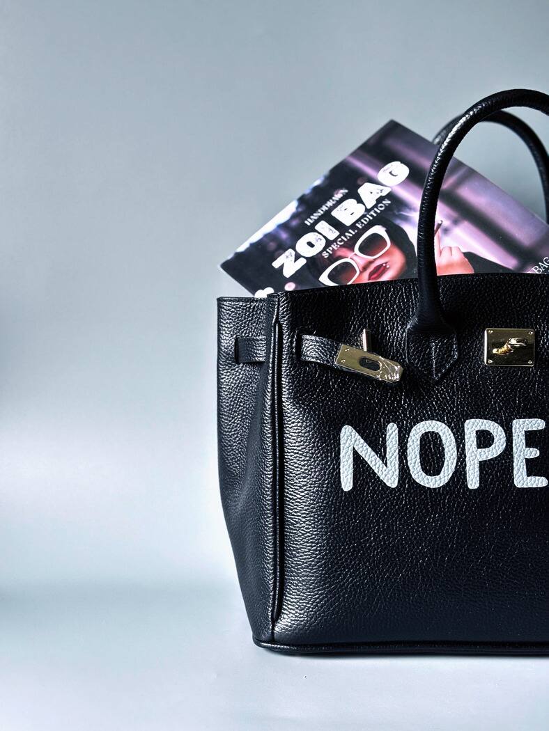 Černá kožená kabelka Zoi Bag s ručně psaným nápisem z pravé italské kůže se zapínáním pomocí ikonického zámku s klíčkem. Detail nápisu.