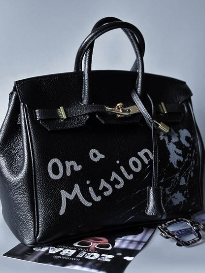 Velká černá kožená kabelka Zoi Bag s ručně psaným nápisem "On a Mission" zapnutá