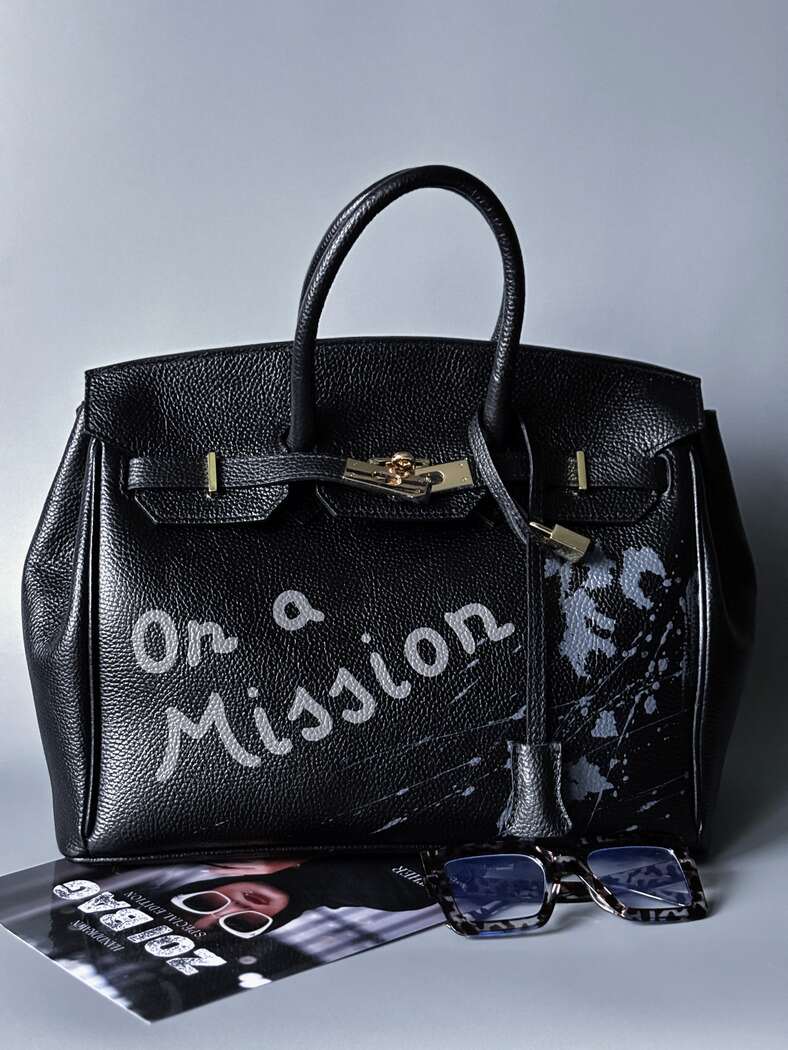 Velká černá kožená kabelka Zoi Bag s ručně psaným nápisem "On a Mission" a s cákanci - zapnutá