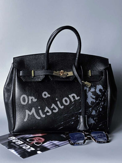 Velká černá kožená kabelka Zoi Bag s ručně psaným nápisem "On a Mission" a s cákanci - zapnutá