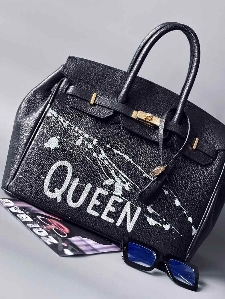 Designová luxusní kožená kabelka Zoi Bag s ručně psaným nápisem "Queen"a s cákanci barvou. Zapínání pomocí zámku a klíčku. Zapnutá.