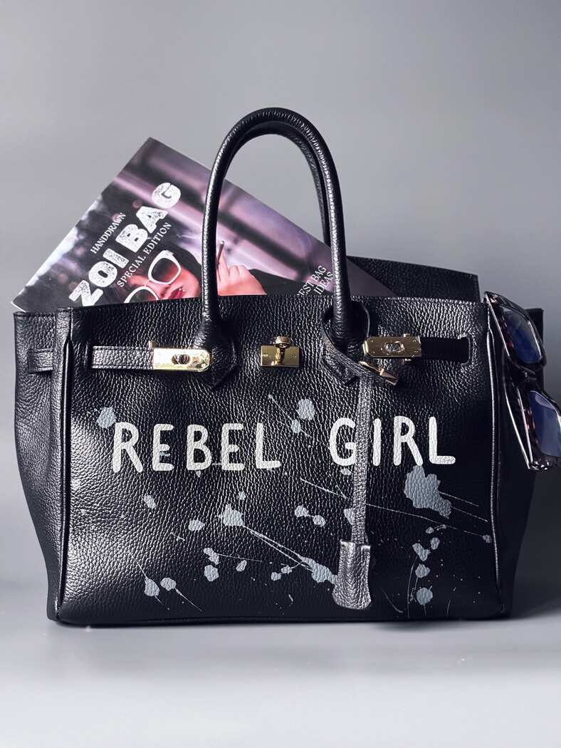 Designová černá kožená kabelka Zoi Bag s ručně psaným nápisem "Rebel Girl" a cákanci barvou. Zámek s klíčkem na zapnutí kabelky.