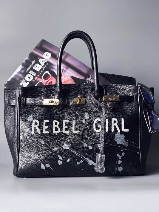 Designová černá kožená kabelka Zoi Bag s ručně psaným nápisem "Rebel Girl" a cákanci barvou. Zámek s klíčkem na zapnutí kabelky.