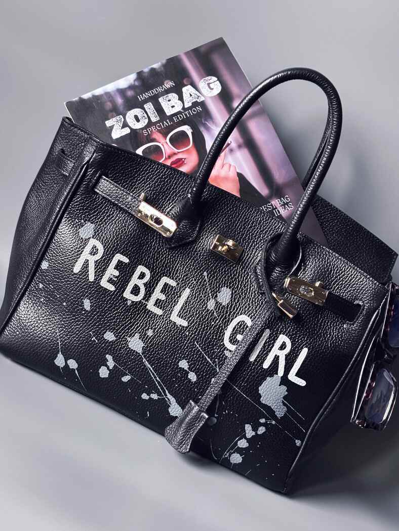Designová černá kožená kabelka Zoi Bag s ručně psaným nápisem "Rebel Girl" a cákanci barvou. Zámek s klíčkem na zapnutí kabelky.