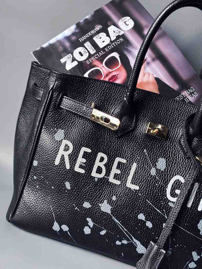 Designová černá kožená kabelka Zoi Bag s ručně psaným nápisem "Rebel Girl" a cákanci barvou. Zámek s klíčkem na zapnutí kabelky.