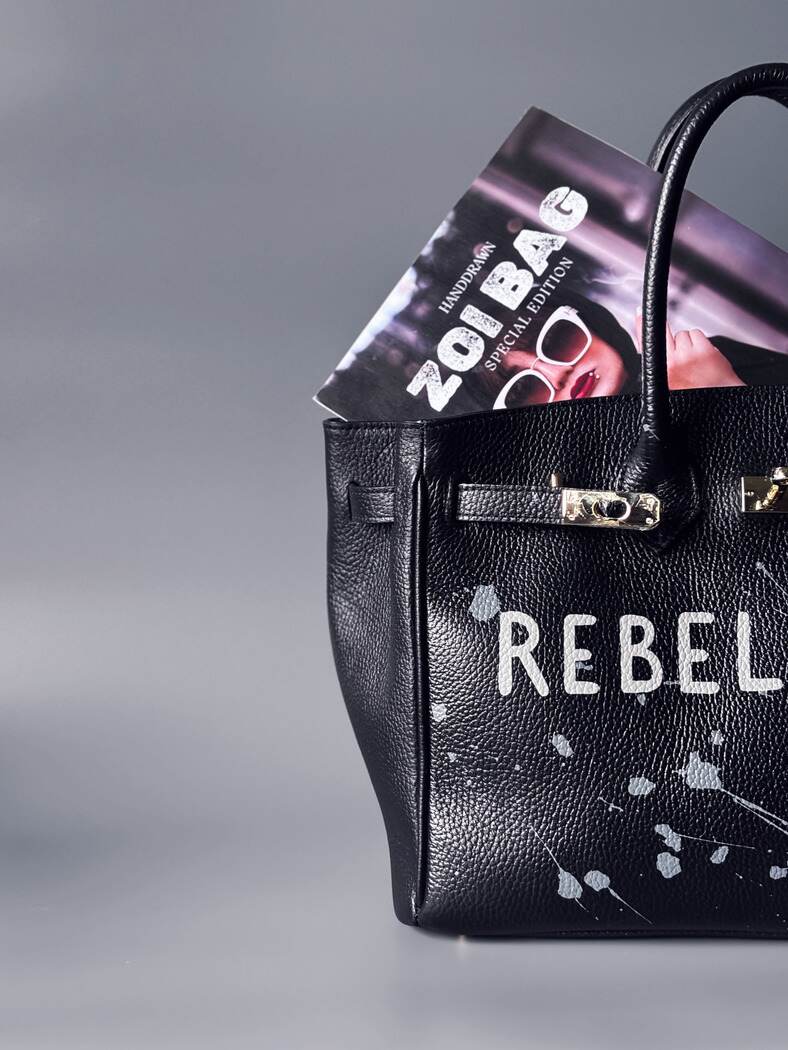 Designová černá kožená kabelka Zoi Bag s ručně psaným nápisem "Rebel Girl" a cákanci barvou. Zámek s klíčkem na zapnutí kabelky.