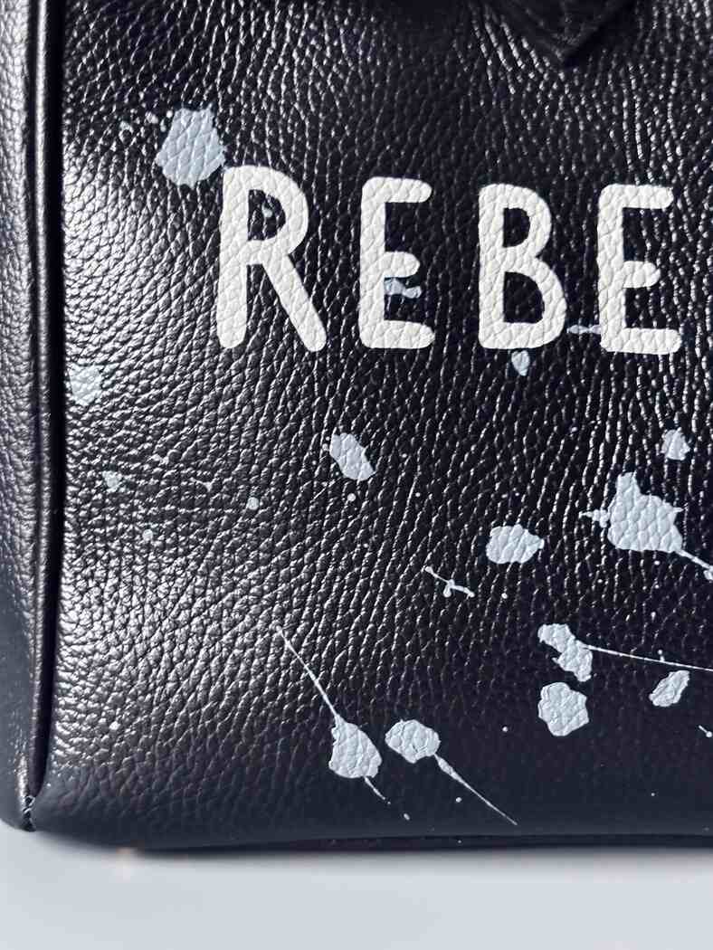Designová černá kožená kabelka Zoi Bag s ručně psaným nápisem "Rebel Girl" a cákanci barvou. Zámek s klíčkem na zapnutí kabelky. Detail.