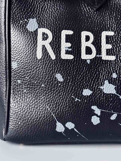 Designová černá kožená kabelka Zoi Bag s ručně psaným nápisem "Rebel Girl" a cákanci barvou. Zámek s klíčkem na zapnutí kabelky. Detail.