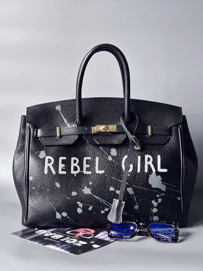 Designová černá kožená kabelka Zoi Bag s ručně psaným nápisem "Rebel Girl" a cákanci barvou. Zámek s klíčkem na zapnutí kabelky.