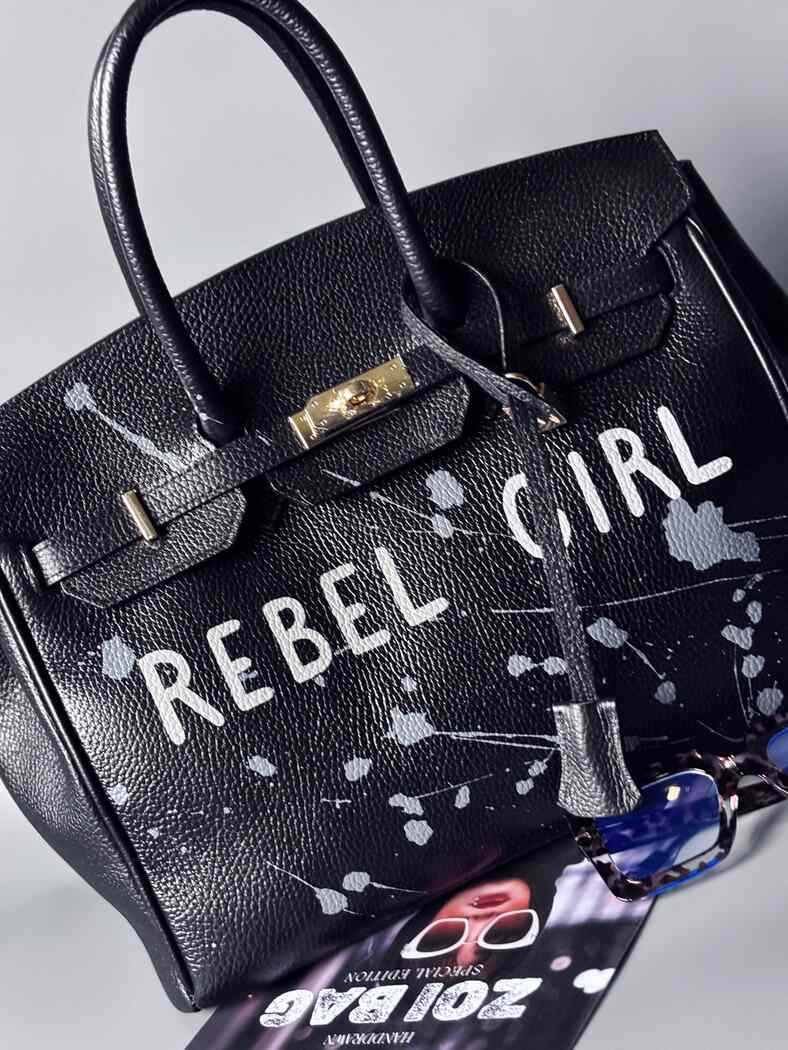 Designová černá kožená kabelka Zoi Bag s ručně psaným nápisem "Rebel Girl" a cákanci barvou. Zámek s klíčkem na zapnutí kabelky. Zapnutá.