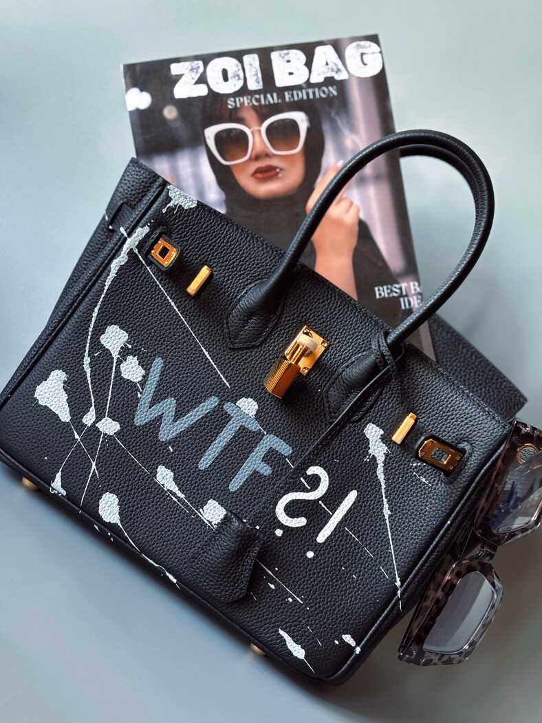 Designová černá kožená kabelka Zoi Bag z právé kůže s ručně psaným nápisem a cákanci barvou. Zlatý zámek s klíčkem.