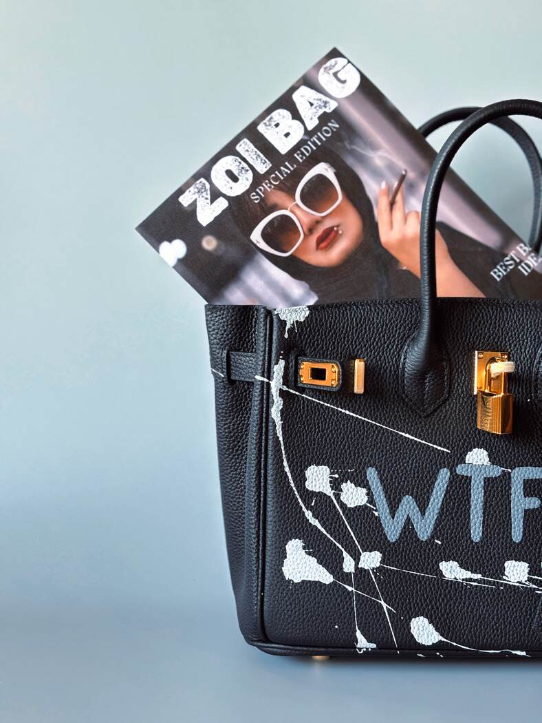 Designová černá kožená kabelka Zoi Bag z právé kůže s ručně psaným nápisem a cákanci barvou. Zlatý zámek s klíčkem. Detail.