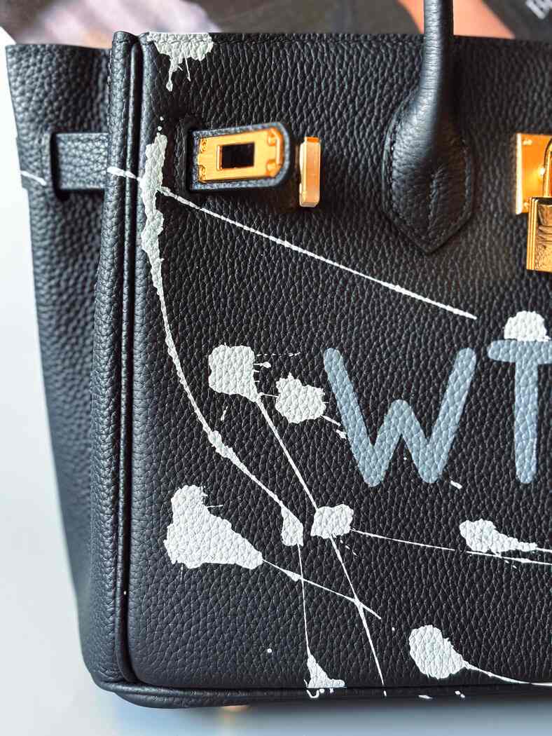 Detail. Designová černá kožená kabelka Zoi Bag z právé kůže s ručně psaným nápisem a cákanci barvou. Zlatý zámek s klíčkem.