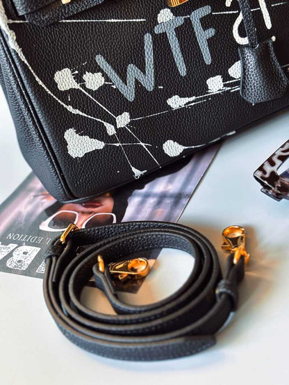 Detail. Designová černá kožená kabelka Zoi Bag z právé kůže s ručně psaným nápisem a cákanci barvou. Zlatý zámek s klíčkem.