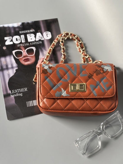 Hnědá kožená kabelka Zoi Bag s ručně psaným nápisem "Love Me" a s cákanci barvu.