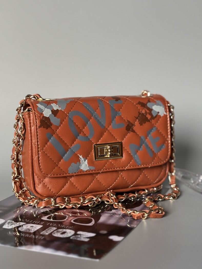 Hnědá kožená kabelka Zoi Bag s ručně psaným nápisem "Love Me" a s cákanci barvu.