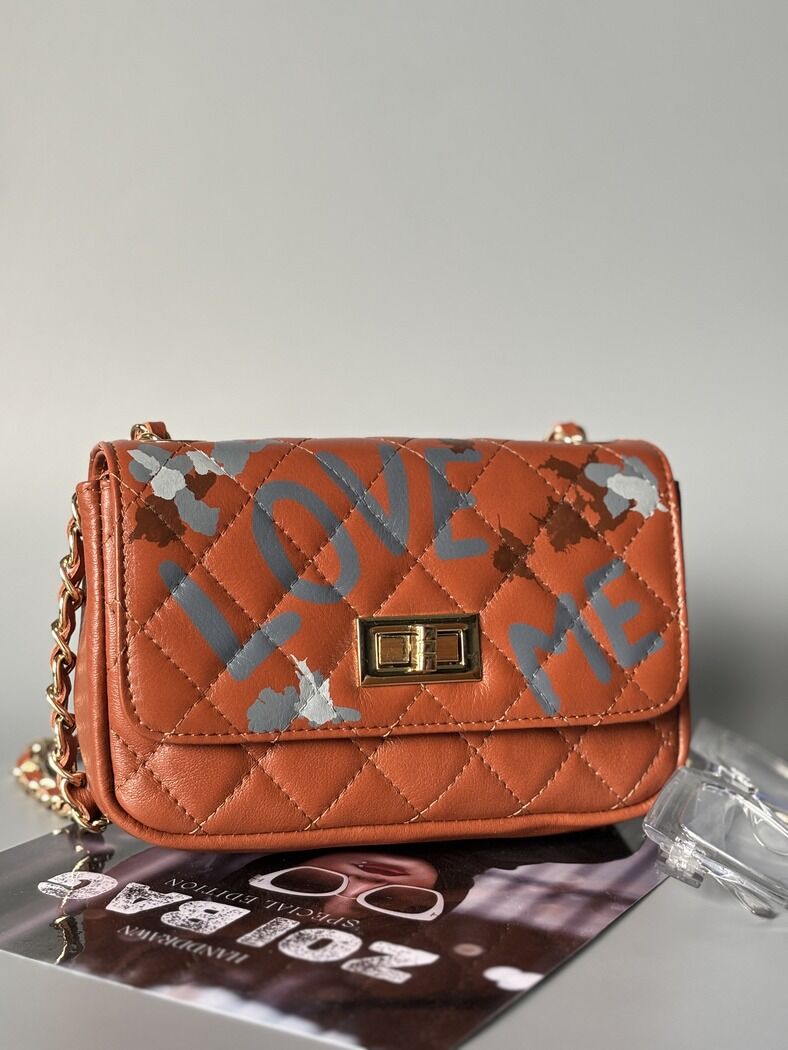 Hnědá kožená kabelka Zoi Bag s ručně psaným nápisem "Love Me" a s cákanci barvu.