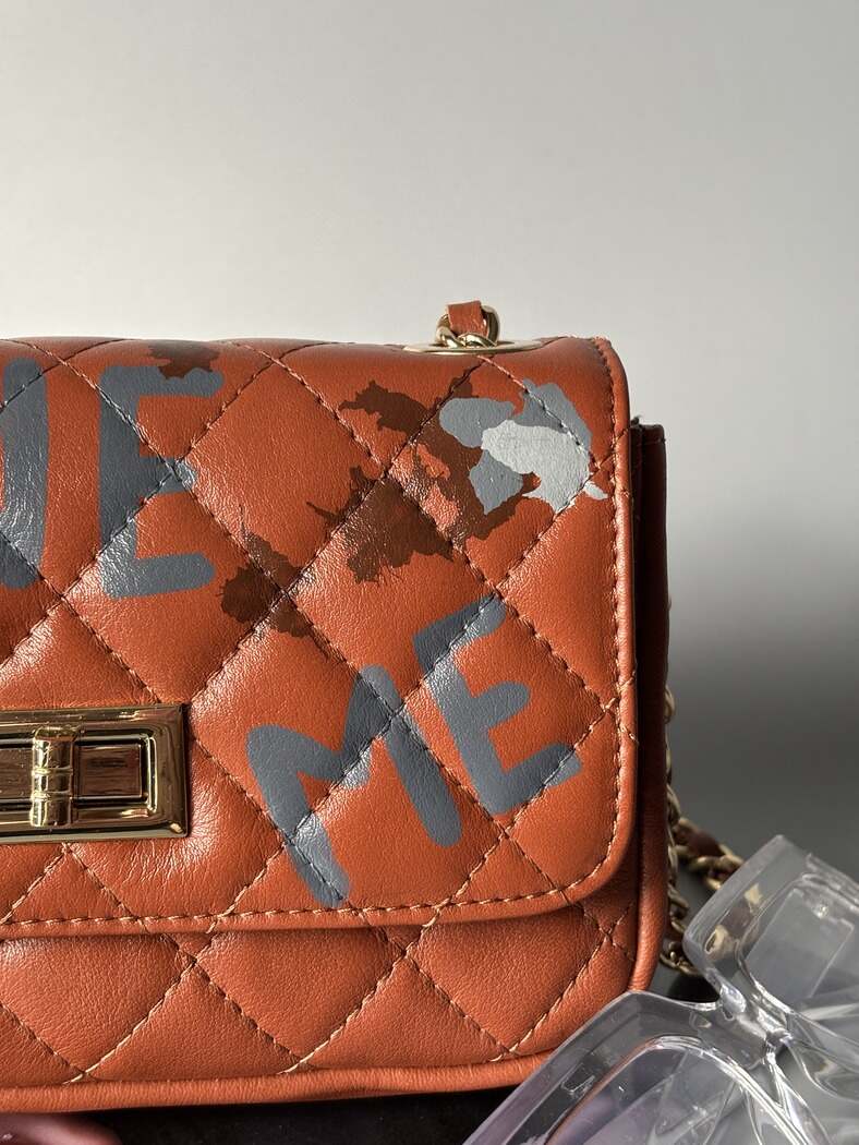 Hnědá kožená kabelka Zoi Bag s ručně psaným nápisem "Love Me" a s cákanci barvu. Detail