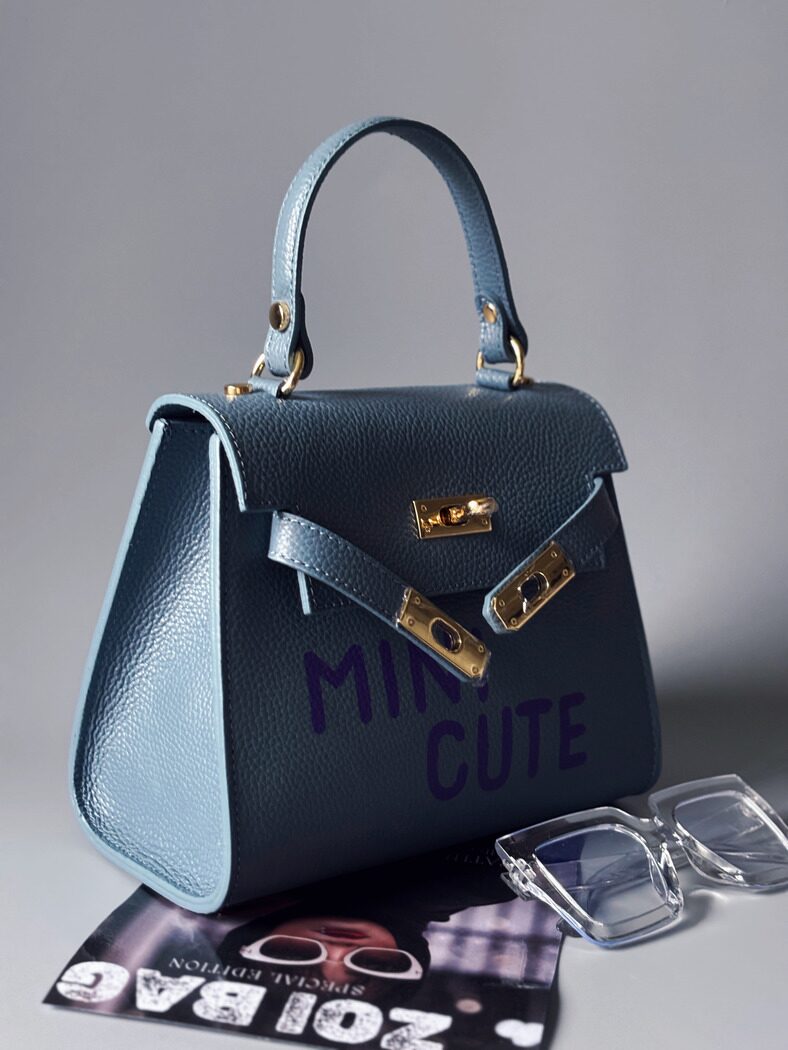 Modrá kožená kabelka Zoi Bag s fialovým nápisem "Mini cute" z boku