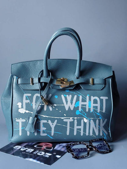 Velká kožená kabelka Zoi Bag v barevné kombinaci modrá a šedá s ručně psaným nápisem "FCK what they think" zapnutá