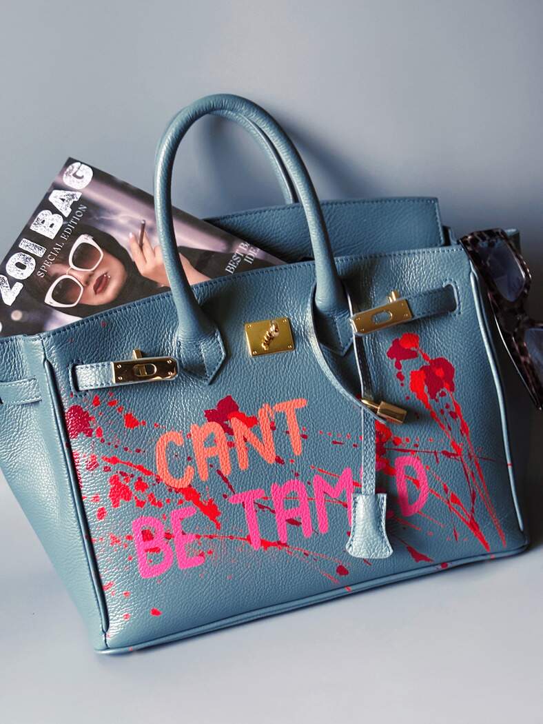 Modrá/šedá kožená kabelka Zoi Bag s ručně psaným nápisem "Can't be tamed" a barevnými cákanci. Doplněna zámkem s klíčkem.