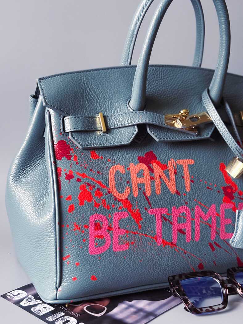 Modrá/šedá kožená kabelka Zoi Bag s ručně psaným nápisem "Can't be tamed" a barevnými cákanci. Doplněna zámkem s klíčkem.