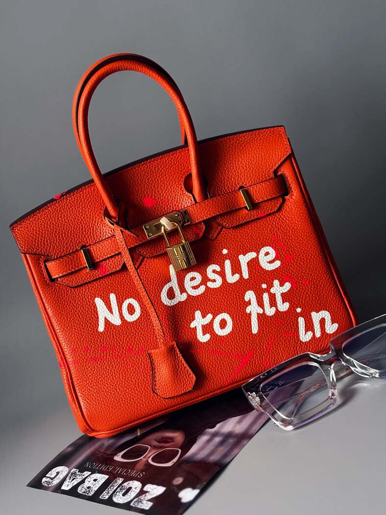 Kožená kabelka Zoi Bag v oranžové barvě s nápisem "No desire to fit in"