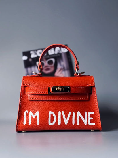 Designová luxusní oranžová kabelka s ručně psaným nápisem, elegantním otočným zámkem a odnímatelným crossbody popruhem.
