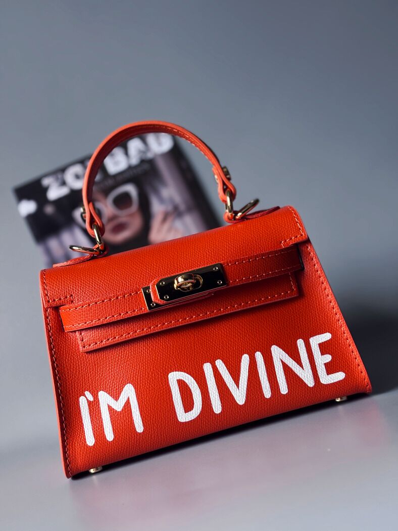 Designová luxusní oranžová kabelka s ručně psaným nápisem, elegantním otočným zámkem a odnímatelným crossbody popruhem.